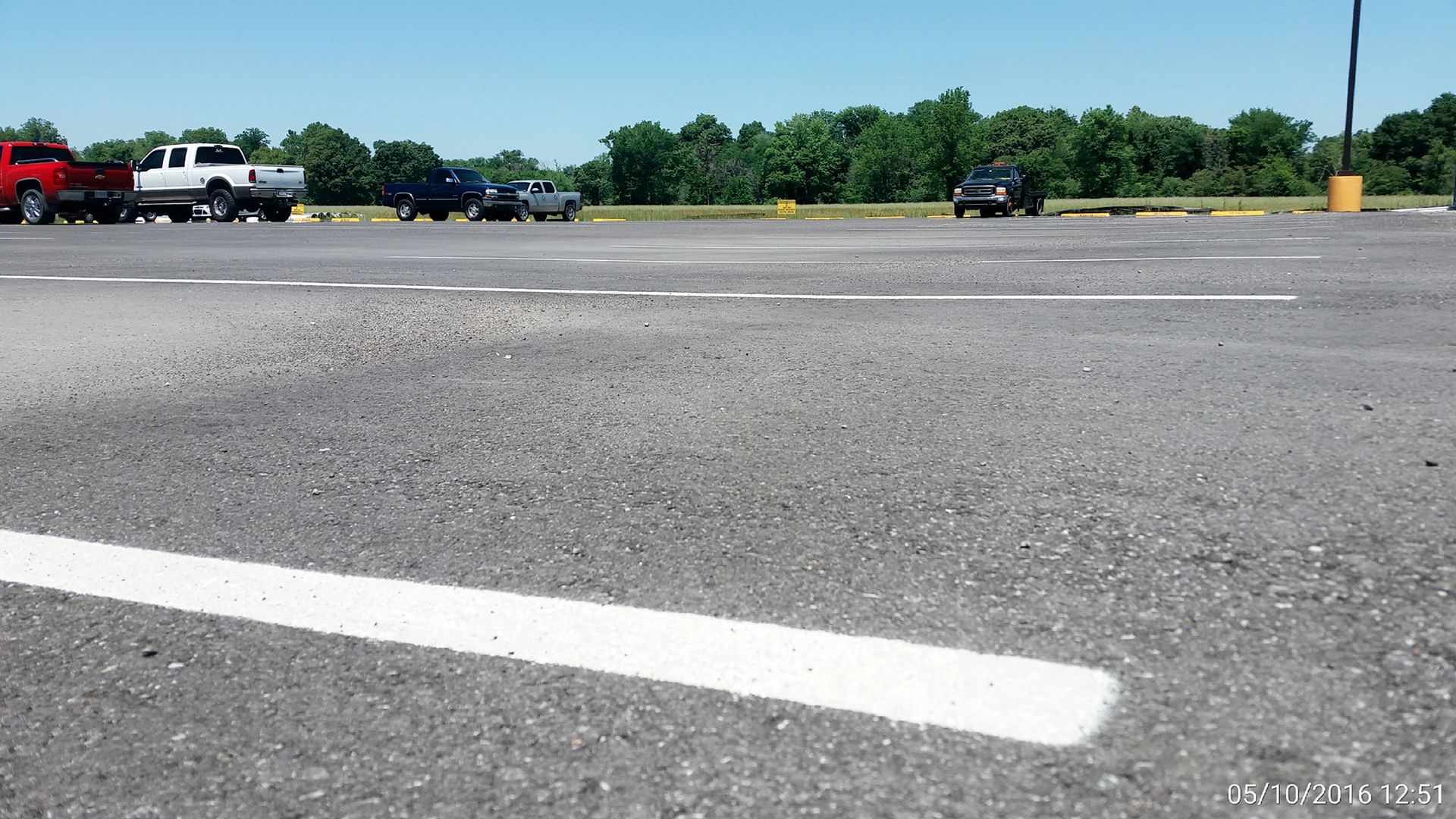 Empty parking lot with white lane markings, trees in the background, and parked trucks along the edge.