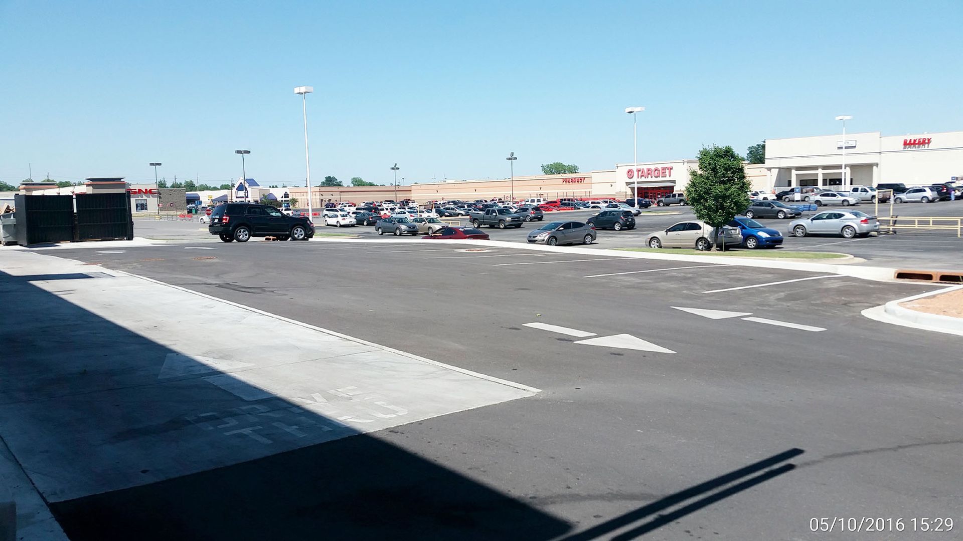 Parking lot outside a strip mall on a sunny day, with cars and storefronts in the distance.