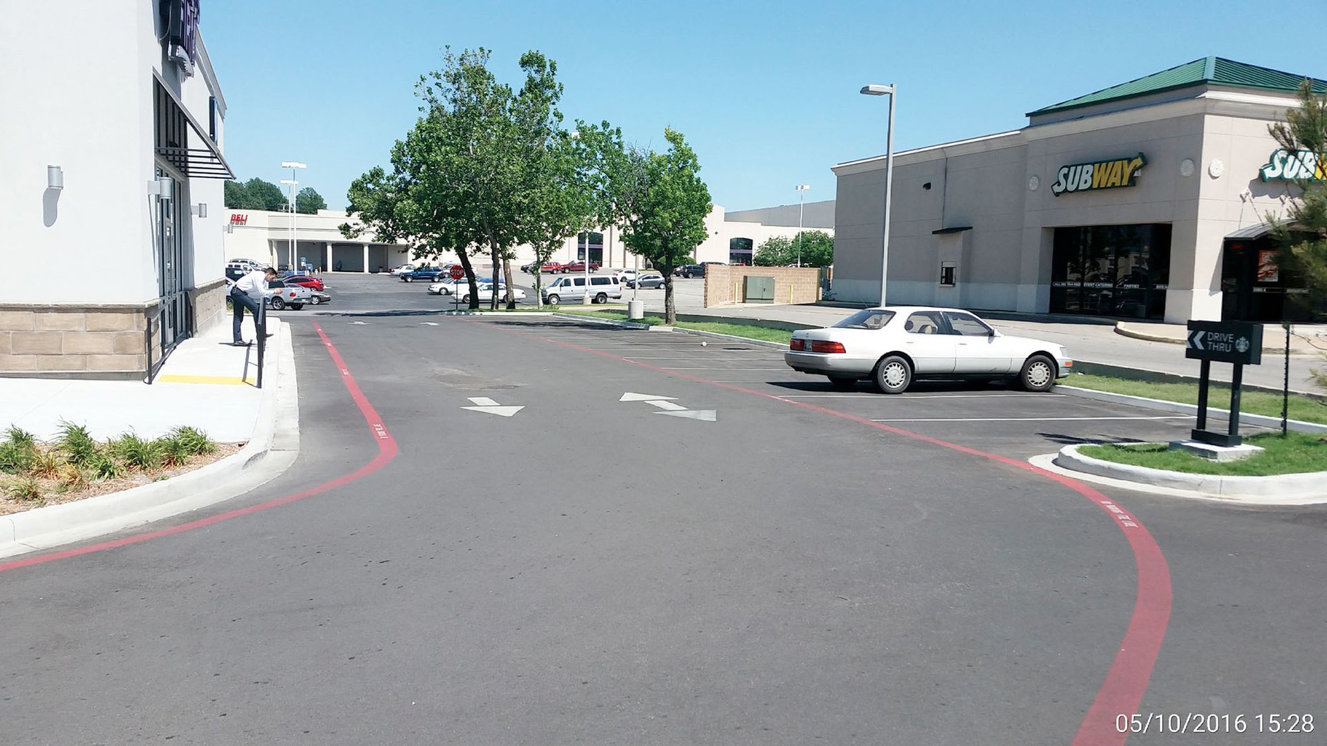 Parking lot with a white car, red curb lines, trees, and buildings on a sunny day