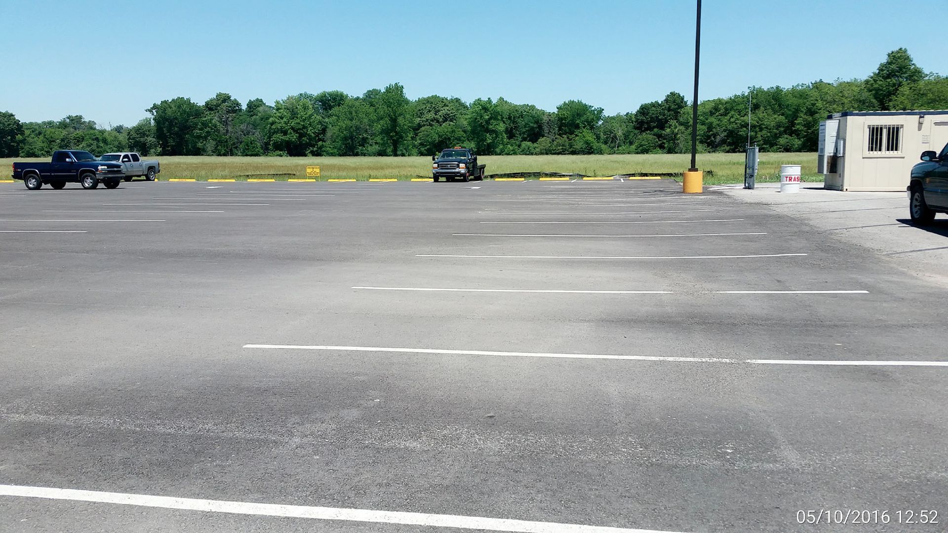 Empty parking lot with a few cars, trees in the distance, and a small booth on the right.