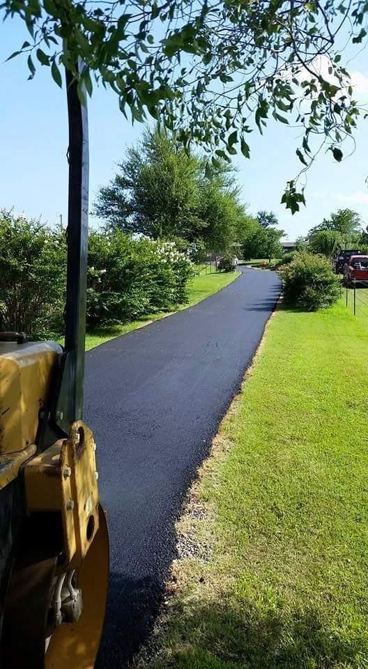 New black paved path curving through a green park, with trees and grass on both sides.