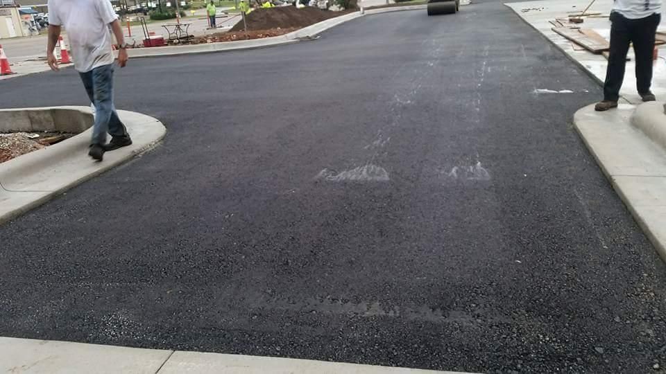Newly paved driveway or road with two people standing on the sidewalks at the sides