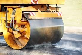 Yellow road roller compacting wet asphalt on a street construction site