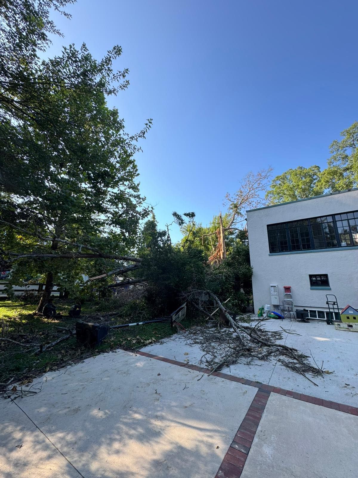 Bright sky with scattered clouds over a building and trees. A concrete driveway is in the foreground. - Before