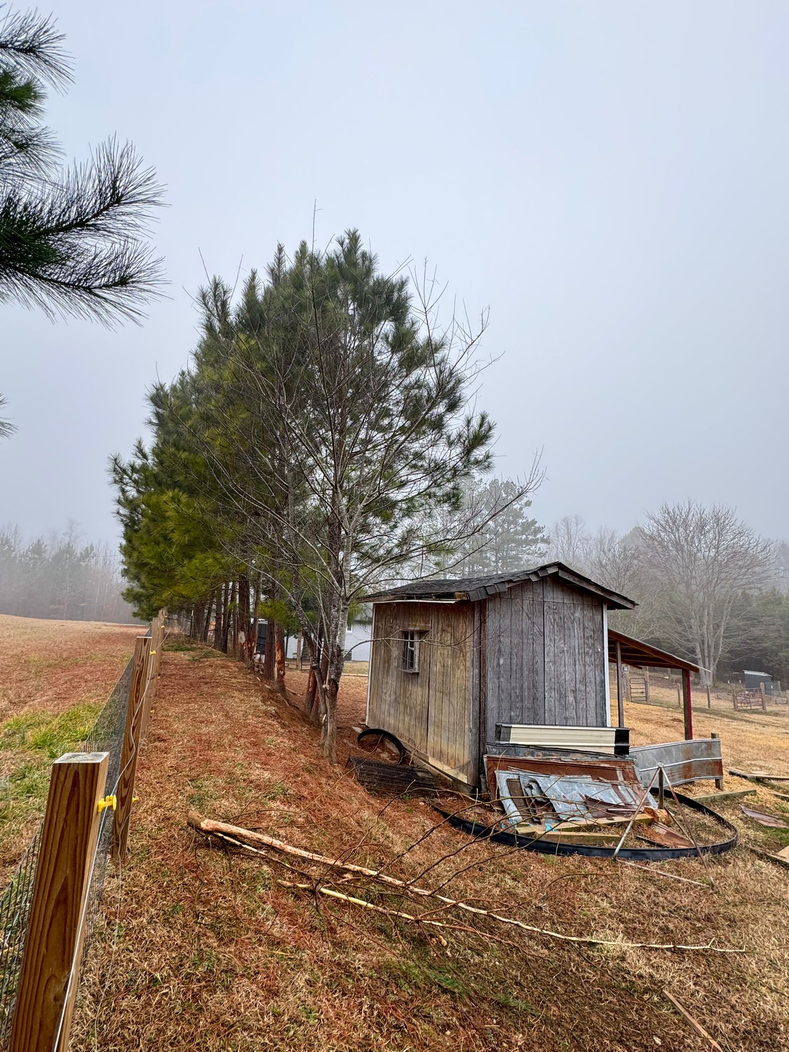 There is a shed in the middle of a field next to a fence.