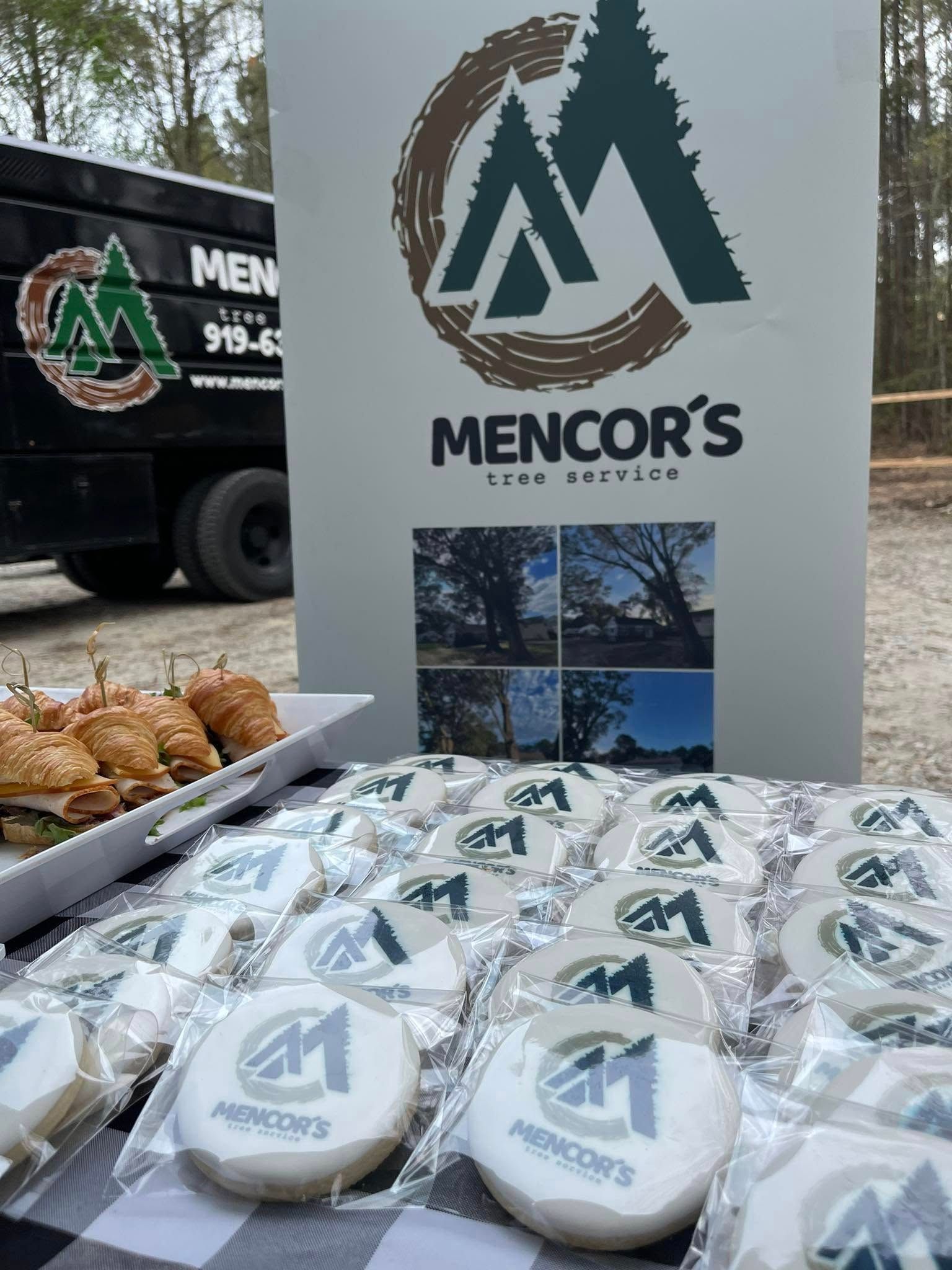 Event with Mencor's Land Services branding: cookies, sandwiches, and a truck with a logo; outdoors in a natural setting.