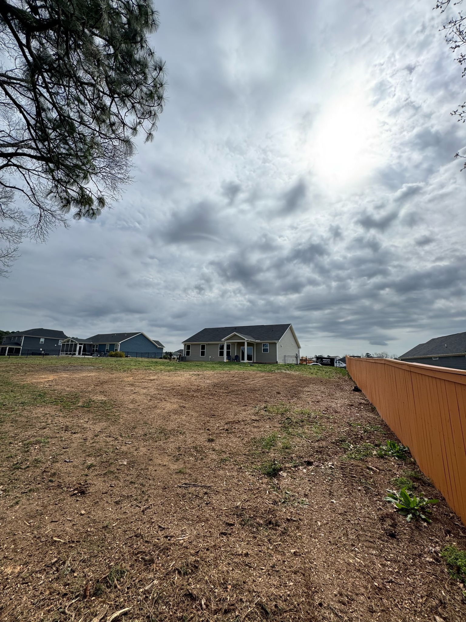 A house is sitting on top of a dirt field next to a fence.