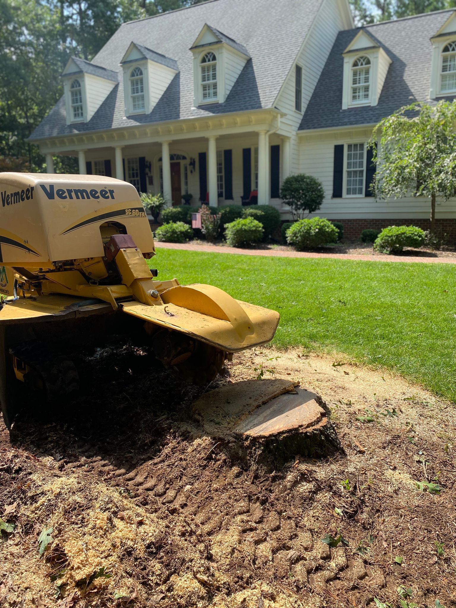 A stump grinder is working on a tree stump in front of a house.