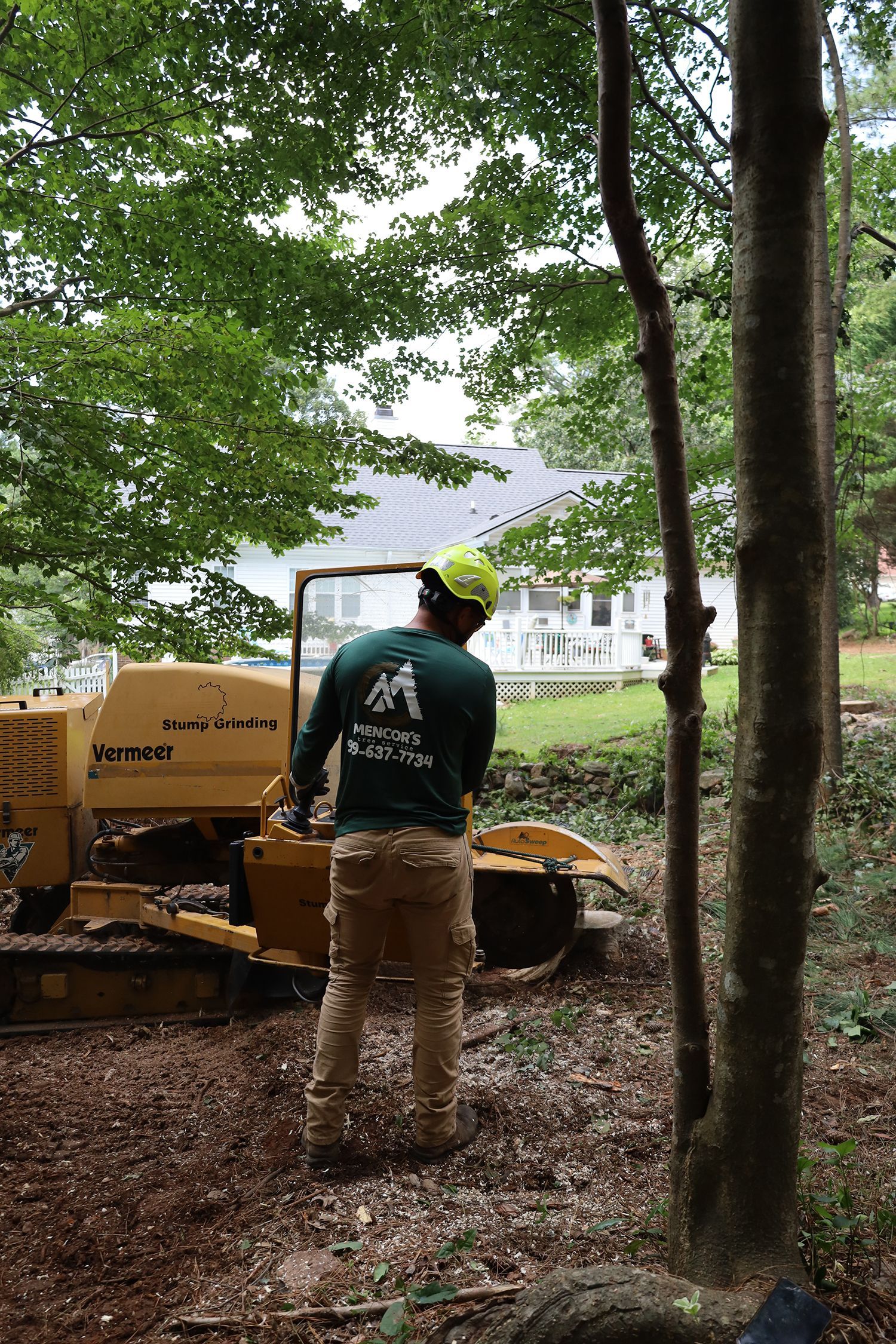 A man is standing next to a yellow tractor in the woods.