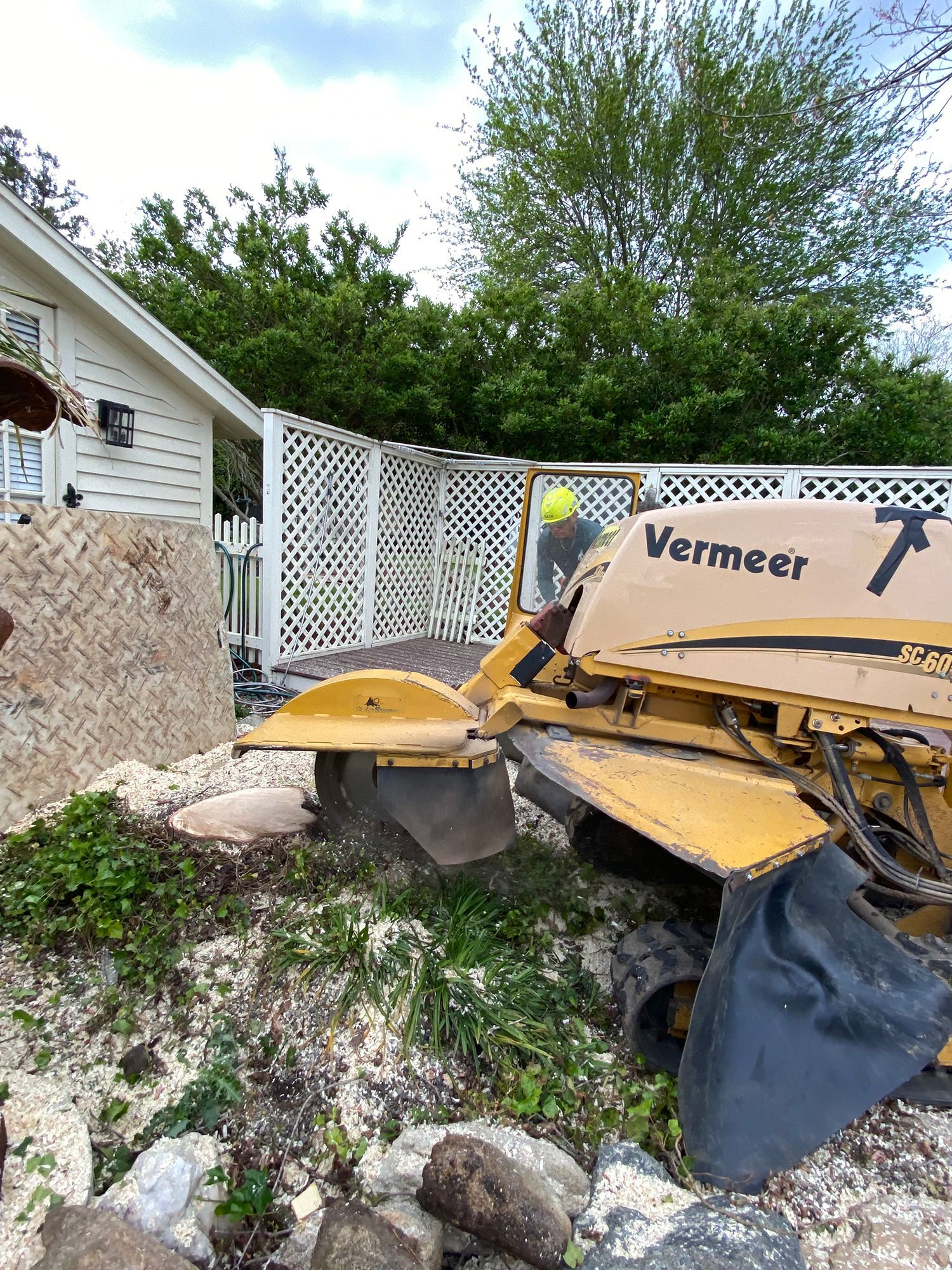 A yellow stump grinder is sitting in front of a house.