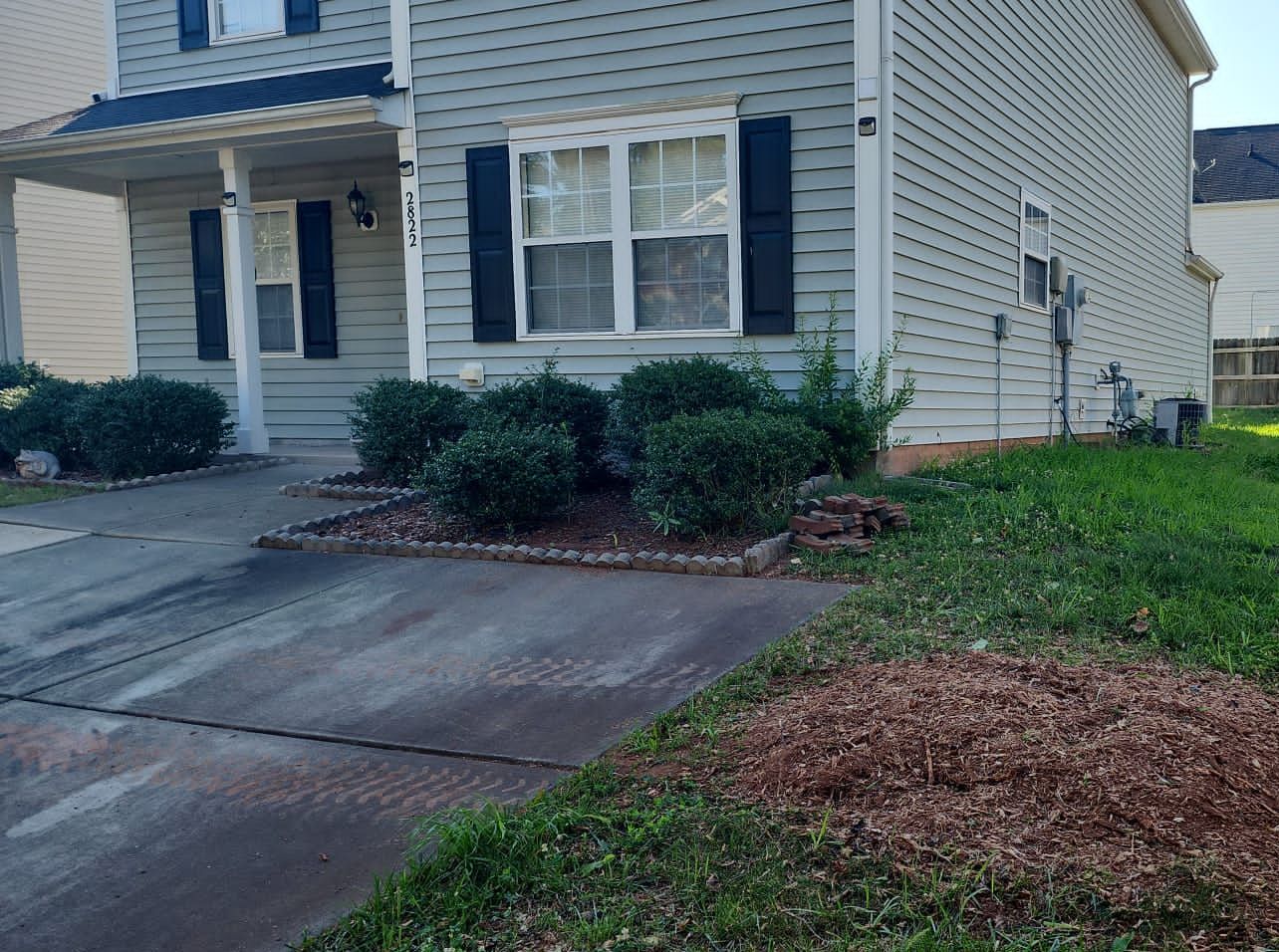 A house with black shutters and a driveway in front of it.