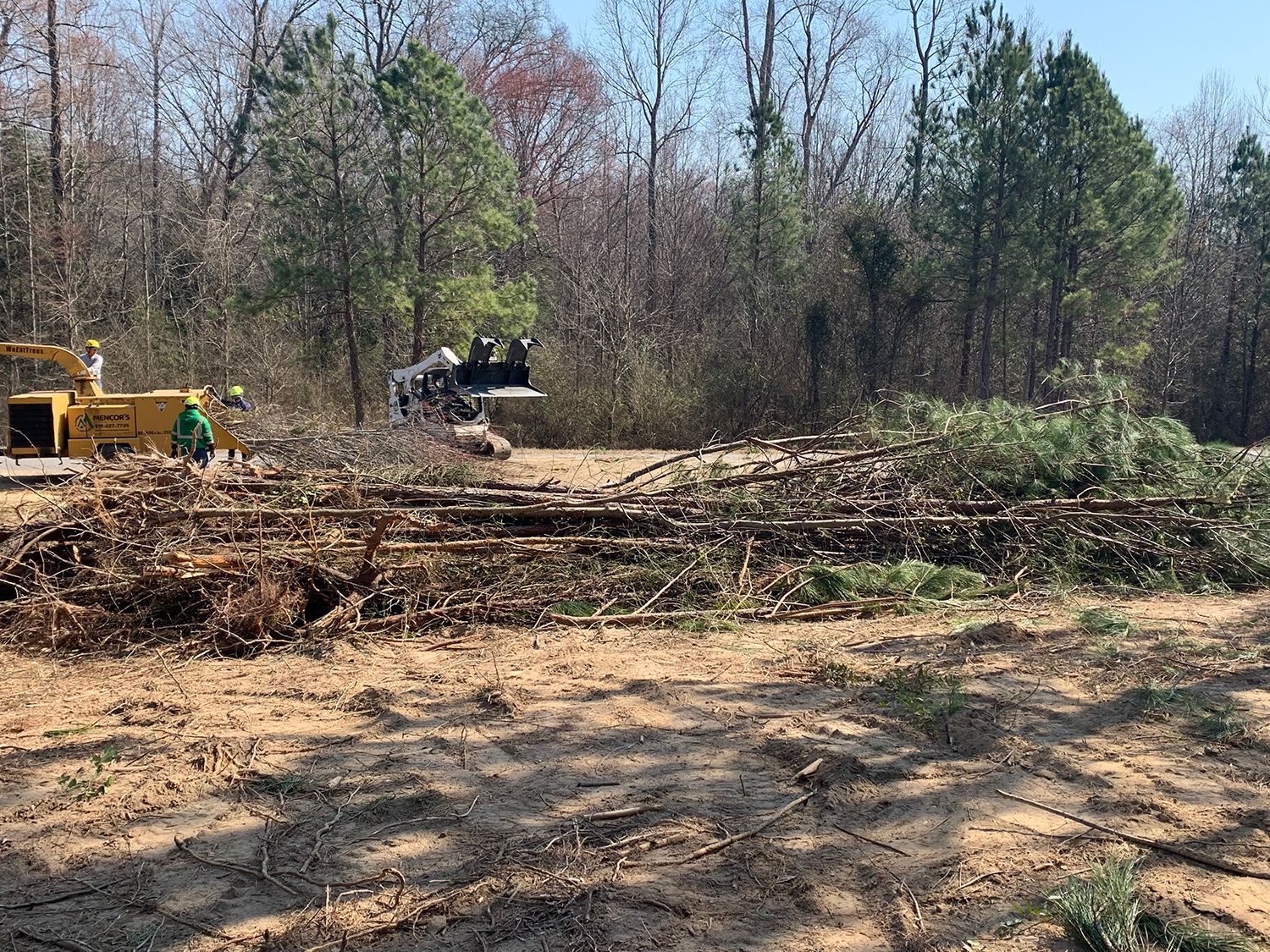 A large pile of logs in a field with a bulldozer in the background.