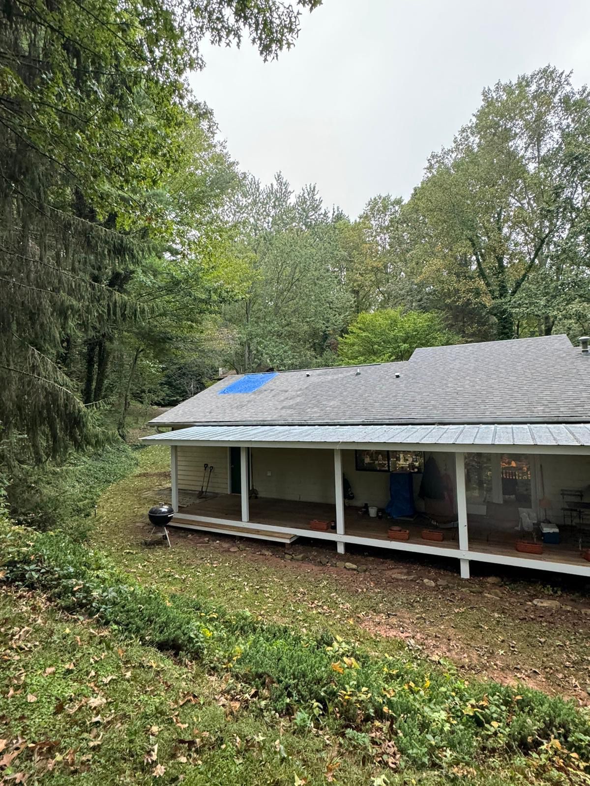 A house with a porch and a roof in the middle of a forest.