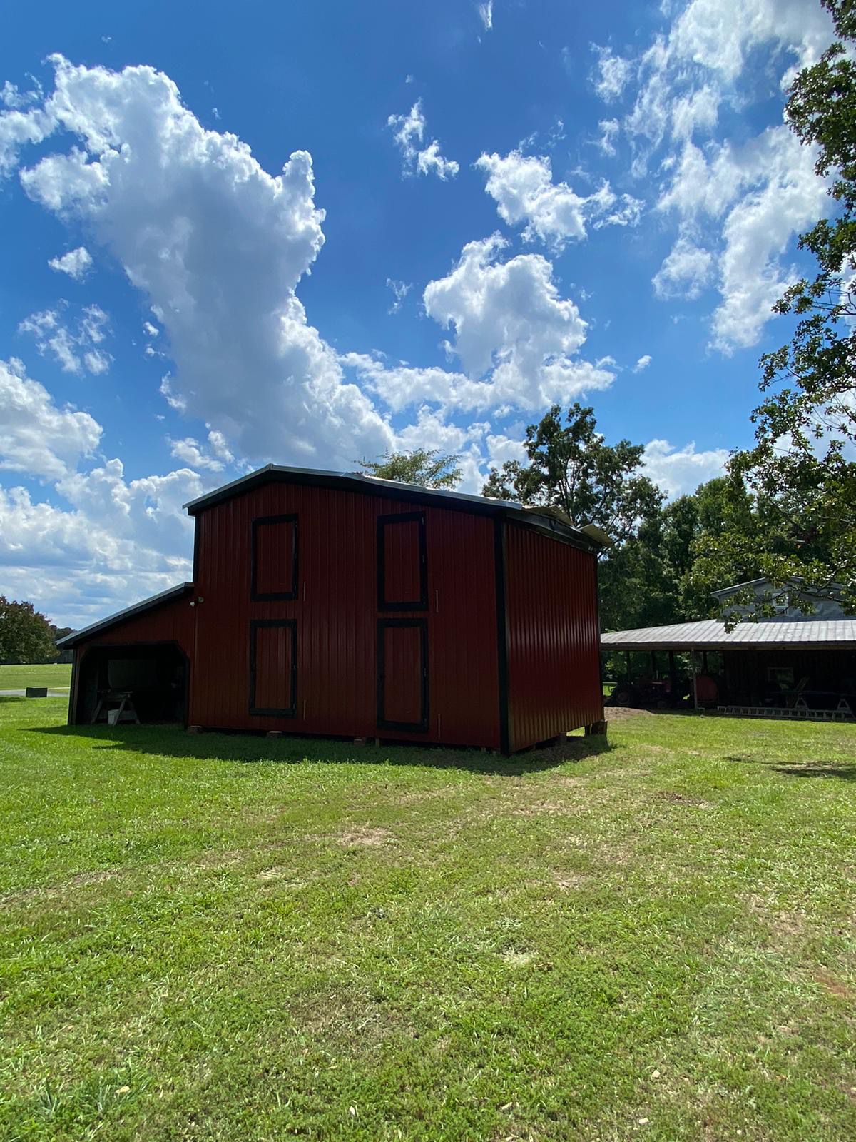 A red barn is sitting in the middle of a grassy field.