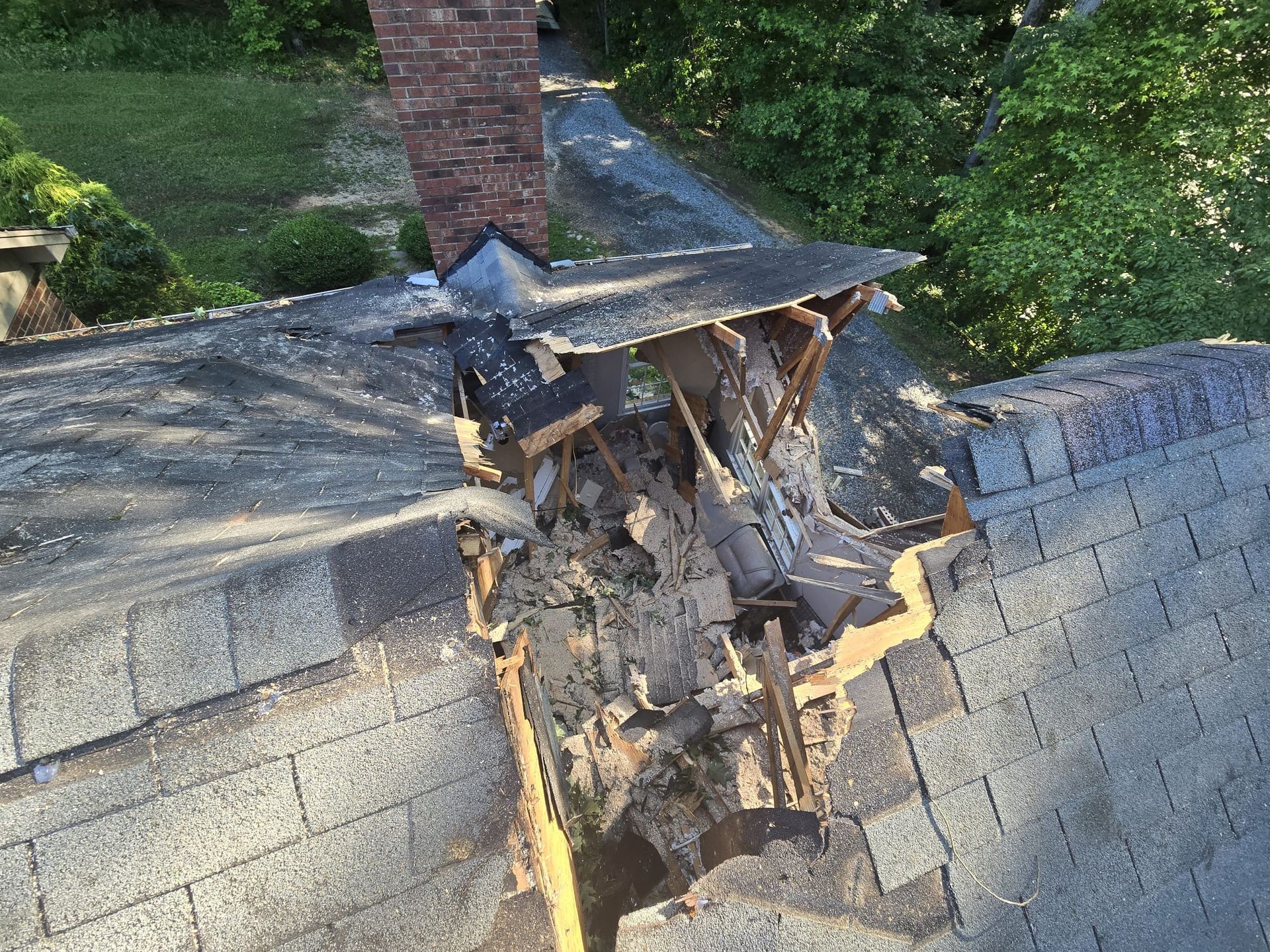 A roof that has been damaged by a tree and a chimney.