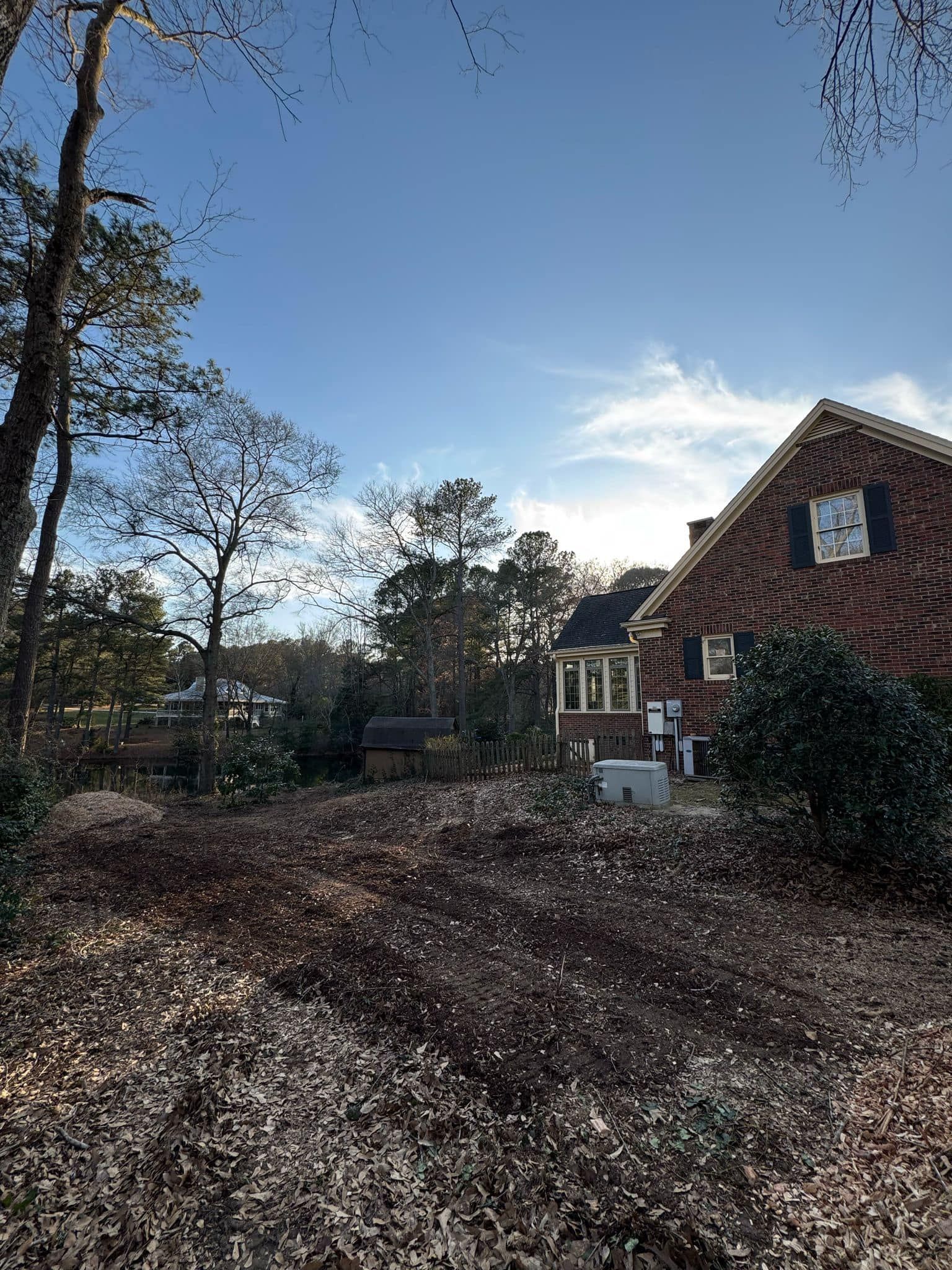 A large brick house is surrounded by trees and leaves on a sunny day.