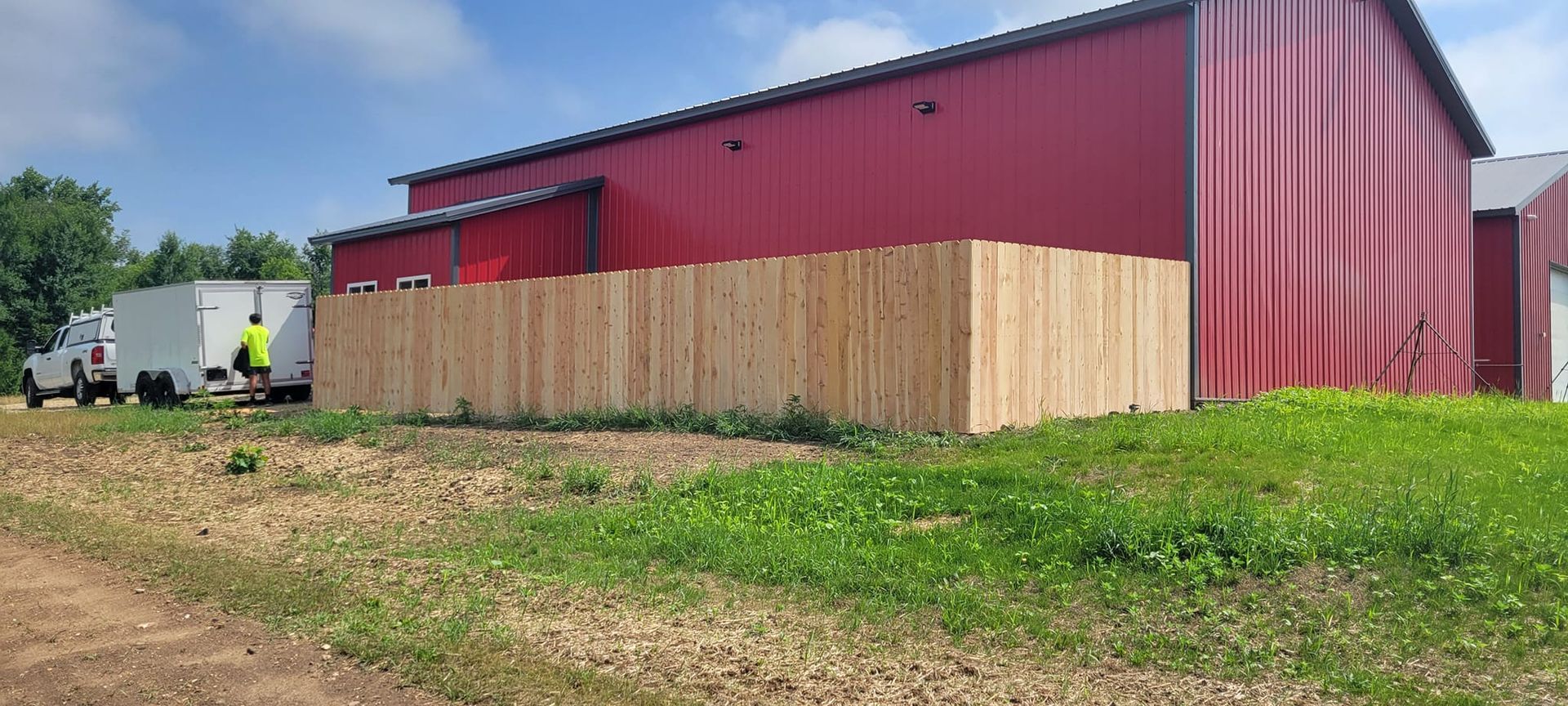 A wooden fence is being built in front of a red barn.