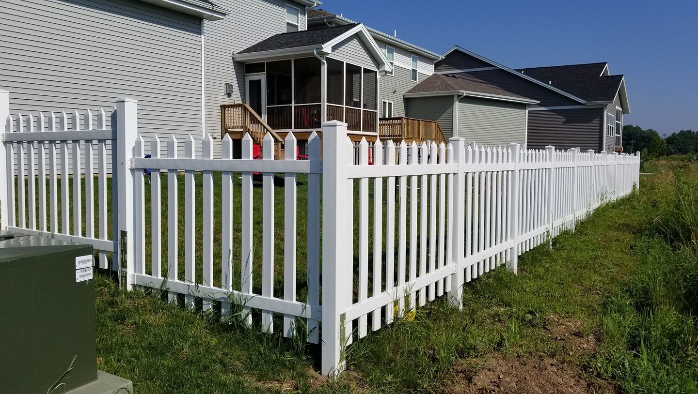 A white picket fence surrounds a house with a screened in porch.