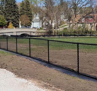 A chain link fence surrounds a field with a bridge in the background