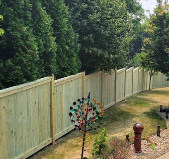 A wooden fence surrounds a backyard filled with trees and a windmill.