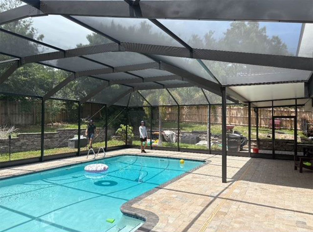 Pool enclosed by a screen. Man stands by pool. Gray frame, blue water, light-colored patio.