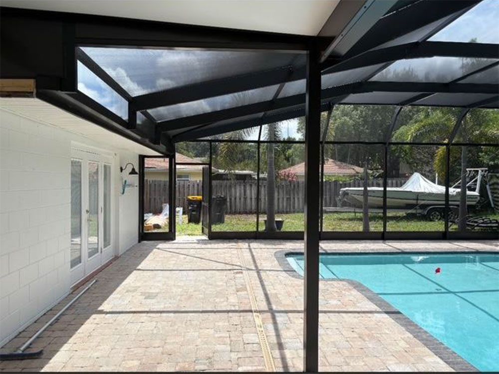 Screened-in pool enclosure with black frame, brick patio, blue pool, and open doors leading to a yard with a boat.