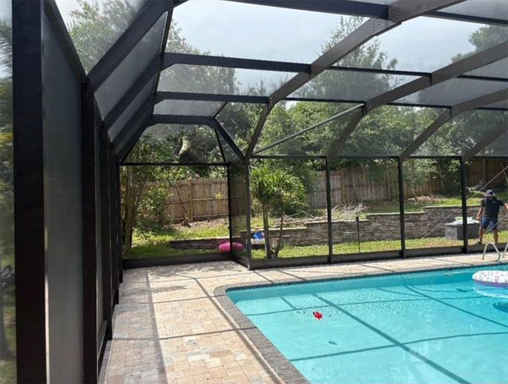 Pool enclosed in a screened lanai, black frame, with brick patio and backyard view.