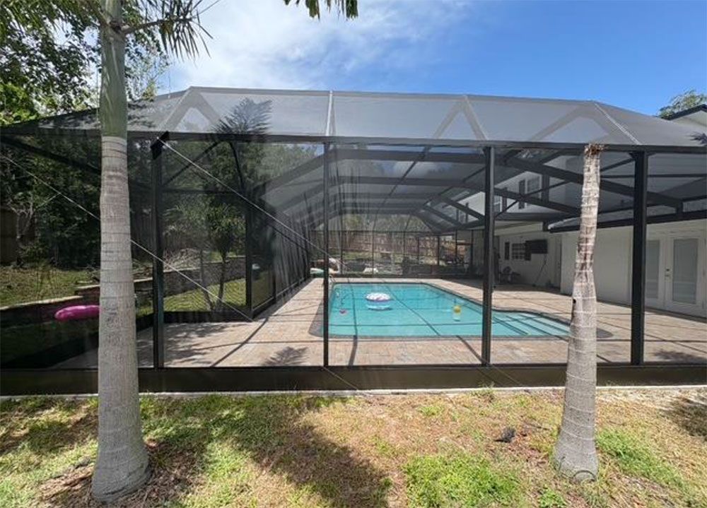 Pool enclosure with black mesh and frame, enclosing a blue pool, under a blue sky.