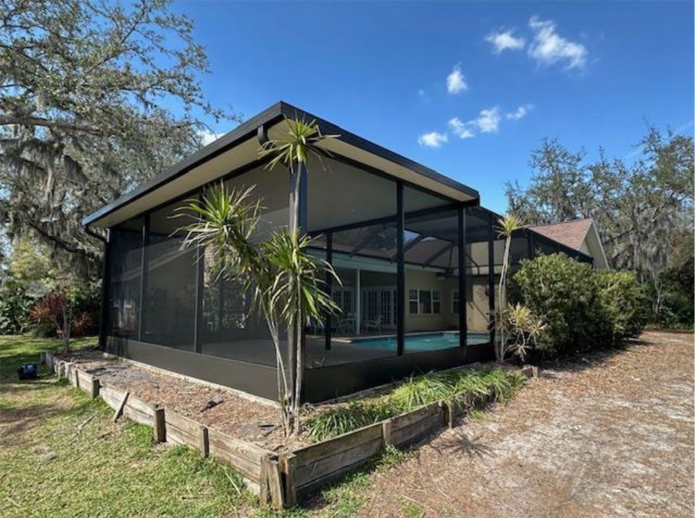 Screened-in pool enclosure with dark frame. Palm trees and foliage. Blue sky, bright day.