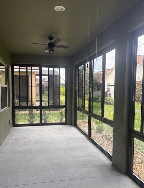 Screened porch with black-framed windows, ceiling fan, and concrete floor overlooking a green yard