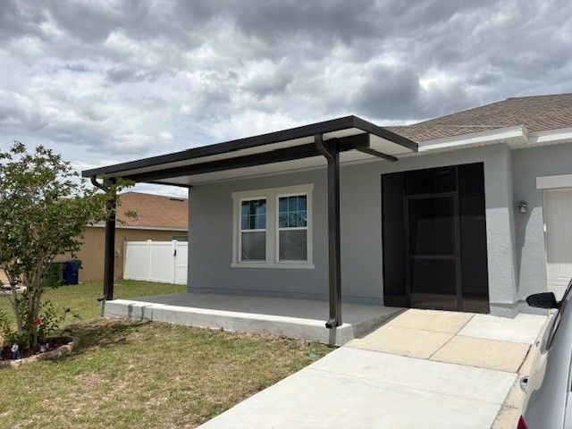Front porch of a gray house with a covered entry and concrete walkway under cloudy skies