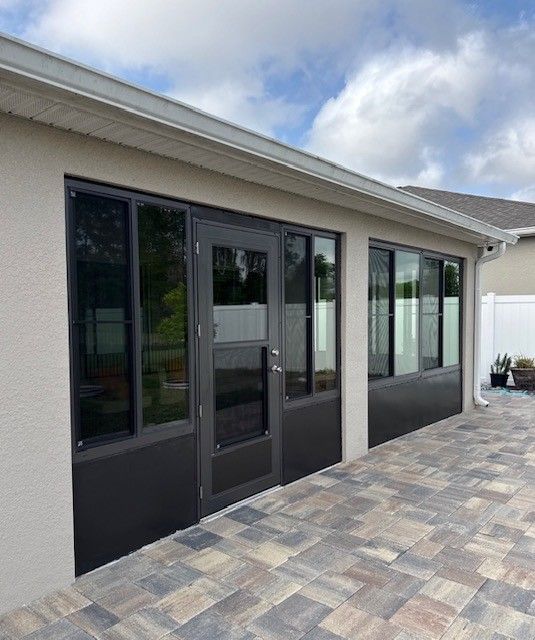 Covered patio with dark-framed glass doors and windows beside a paved stone walkway.