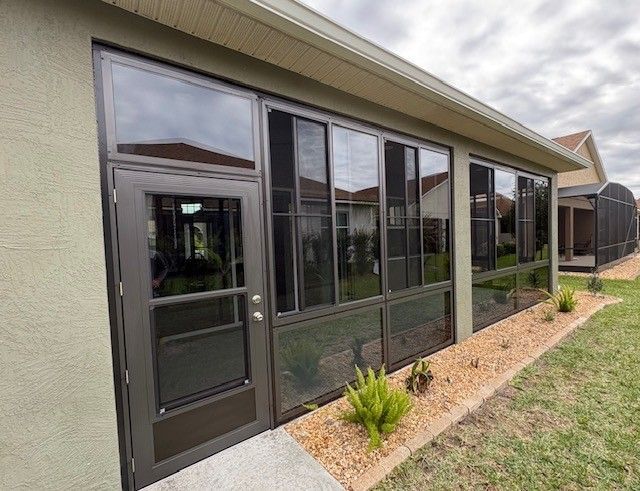 Exterior of a beige house with dark-framed glass doors and windows along a screened patio.