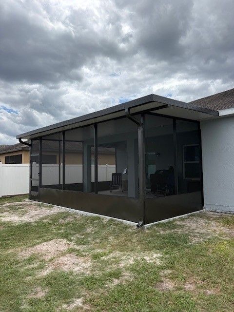 Screened patio enclosure on a house in a grassy backyard under cloudy skies