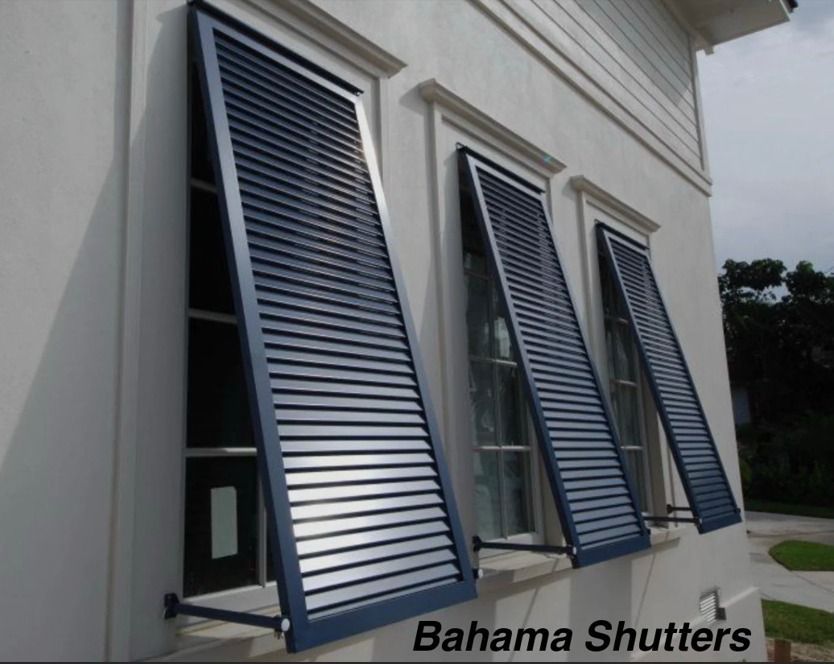 Three blue louvered Bahama shutters open on a white house exterior