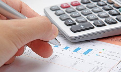 A person is writing on a piece of paper next to a calculator.