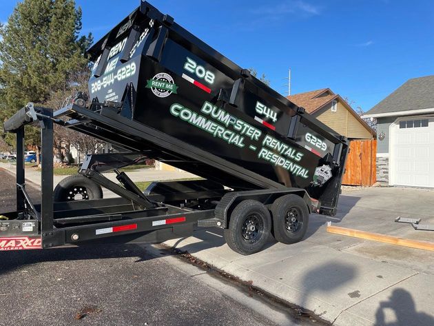 Black dumpster rental truck tilted on a trailer in a residential driveway