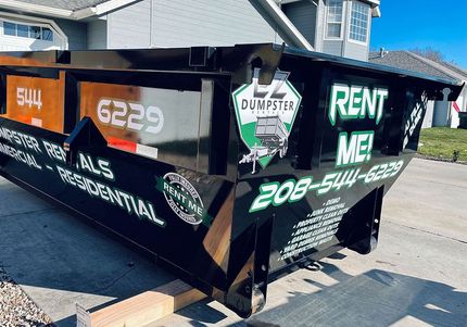 Black dumpster trailer with green RENT ME! graffiti and phone number parked on a street