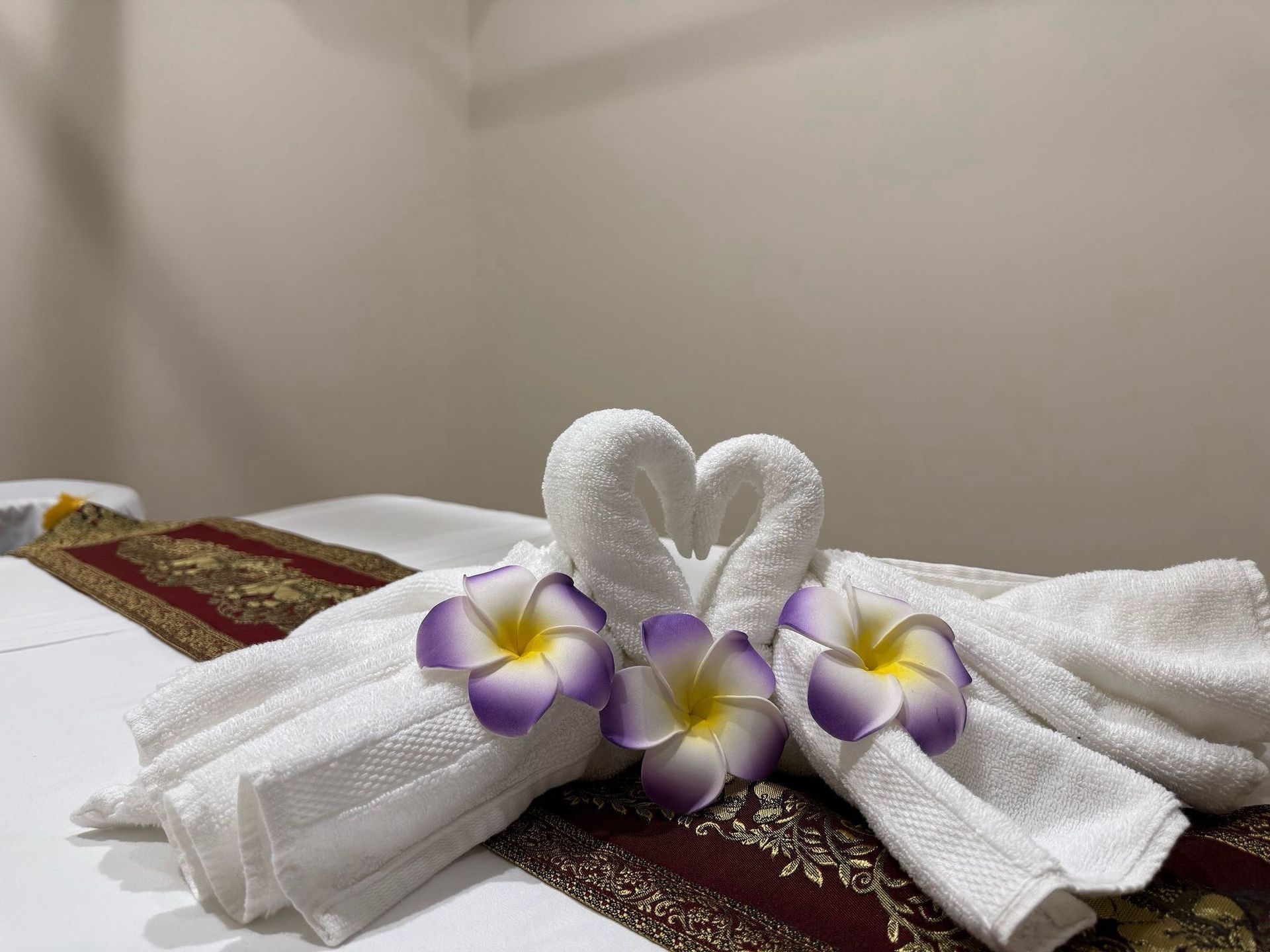 White towels folded into swans, decorated with flowers, on a massage table.