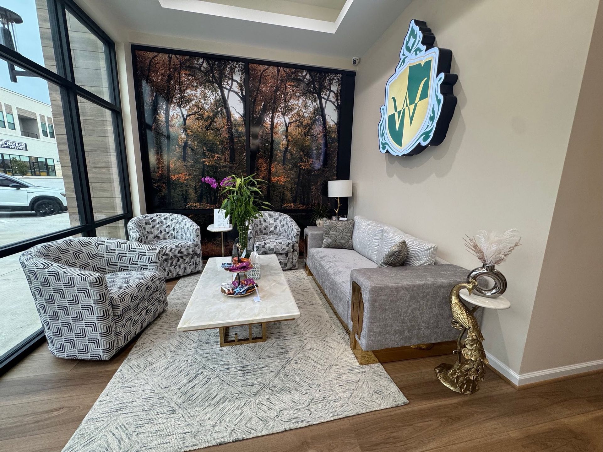 Waiting room with patterned chairs, a sofa, coffee table, and a forest tapestry. Company logo on wall.
