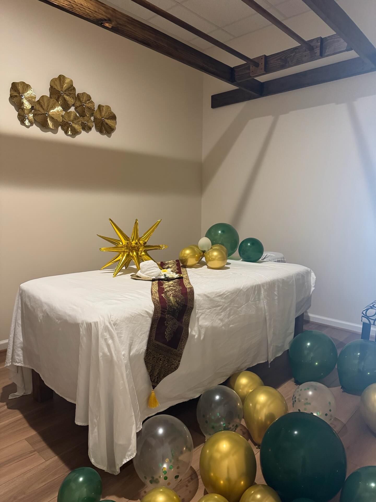 A massage table set for celebration, adorned with balloons, gold decor, and a decorative runner in a room.