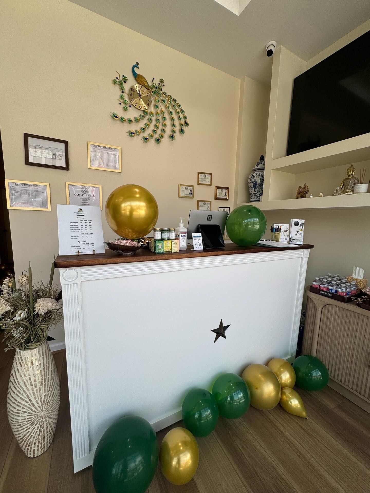 Reception desk decorated with gold and green balloons, peacock art, and framed items.