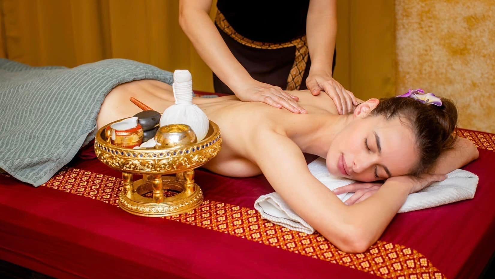 Woman receiving back massage in a spa. Golden tray with tools nearby.