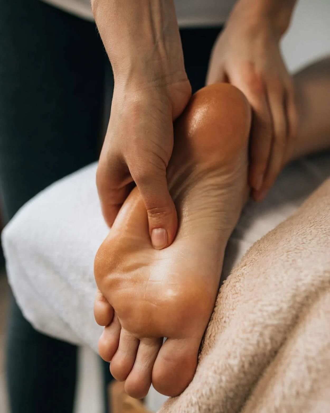 Hands massaging a foot, applying oil; on a white towel.