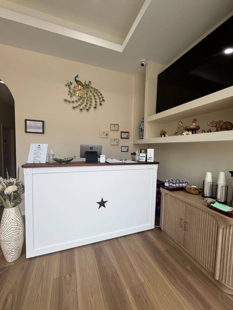 White reception desk in a spa, with a star, peacock wall art, and wood-tone floors.