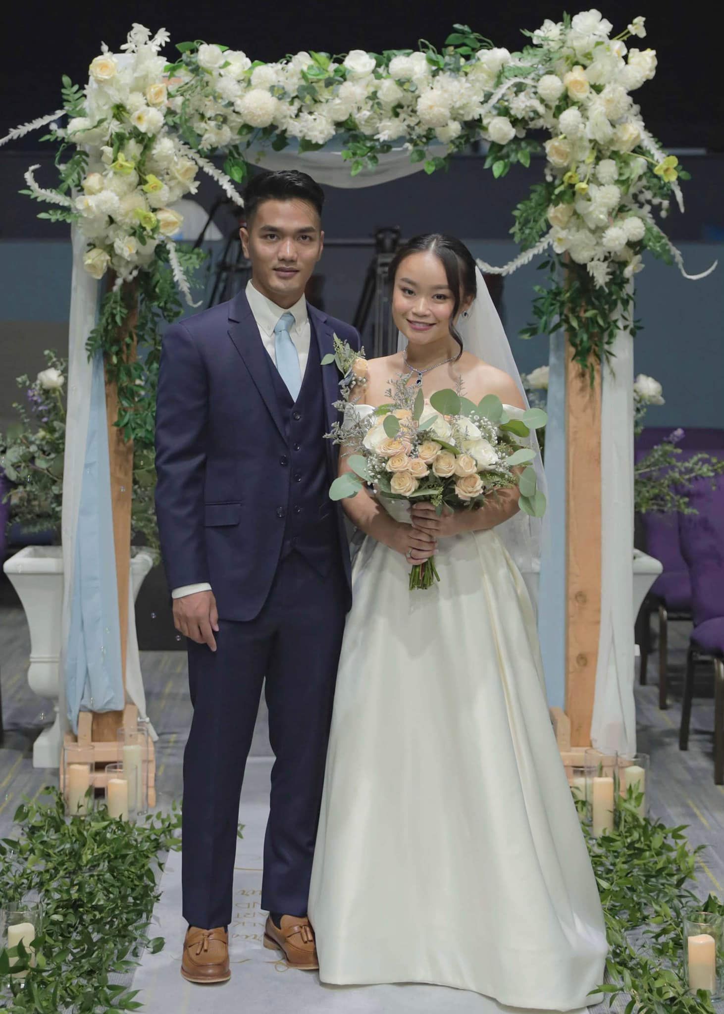A bride and groom are posing for a picture in front of a floral arch.