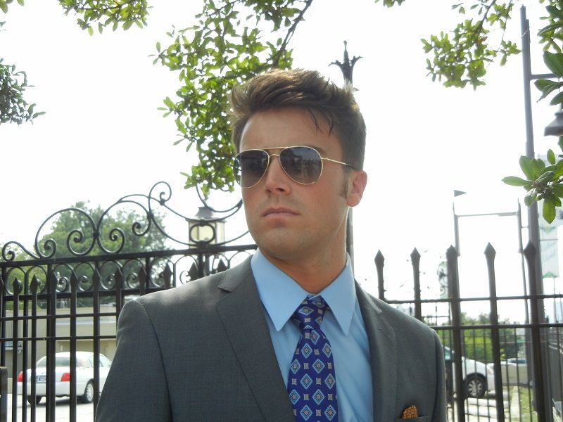 A man in a suit and tie is standing in front of a fence