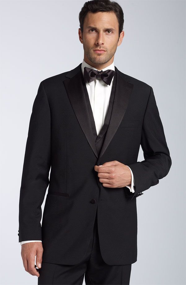 A man is wearing a black tuxedo and bow tie