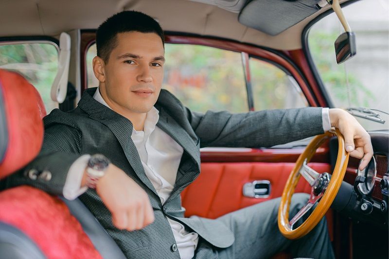 A man in a suit is sitting in the driver 's seat of an old car.