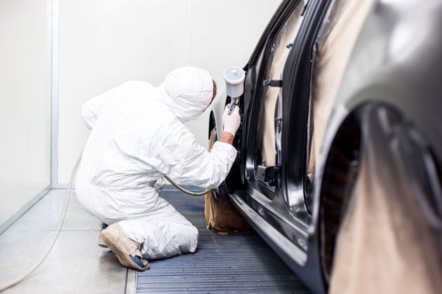 Technician in white protective suit spray-paints a black car in a paint booth